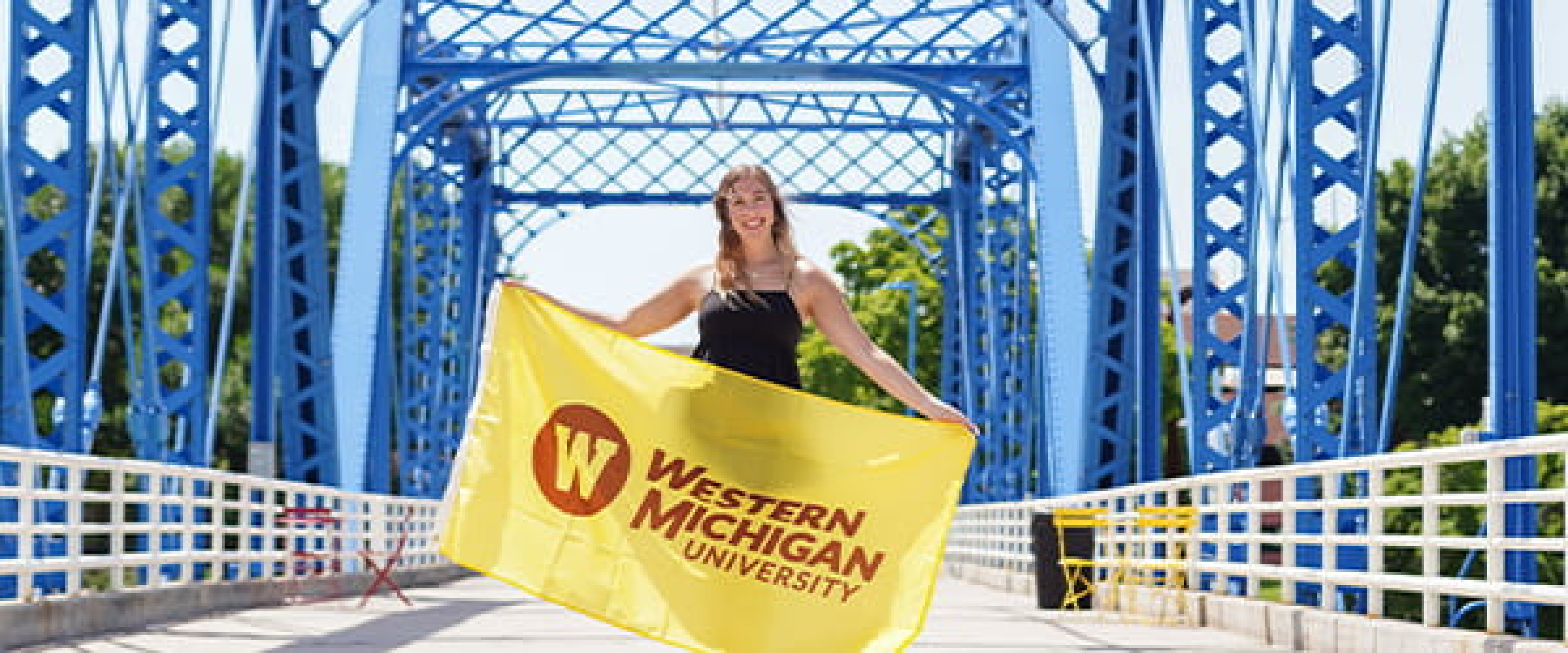 Girl on the blue iron bridge in Grand Rapids holding up a WMU flag
